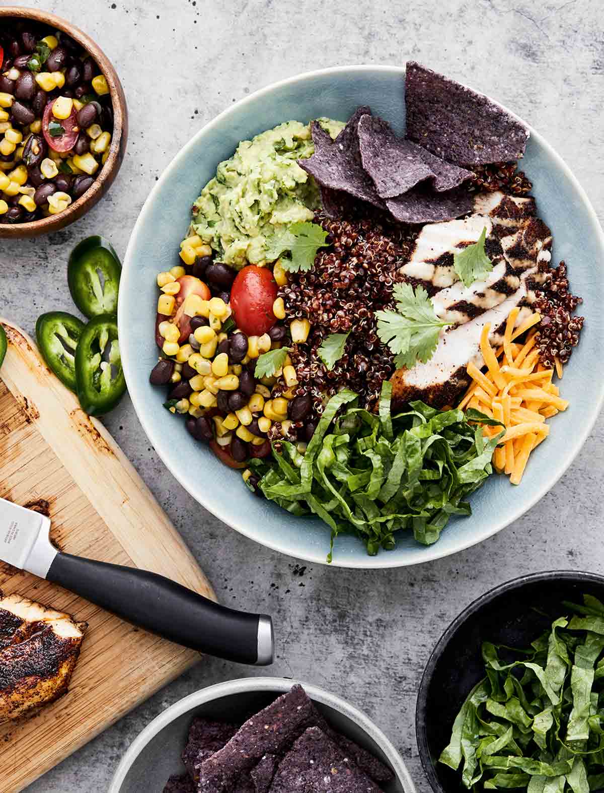 A chicken burrito bowl with grilled chicken, quinoa, lettuce, cheese, corn, beans, guacamole, and purple corn chips