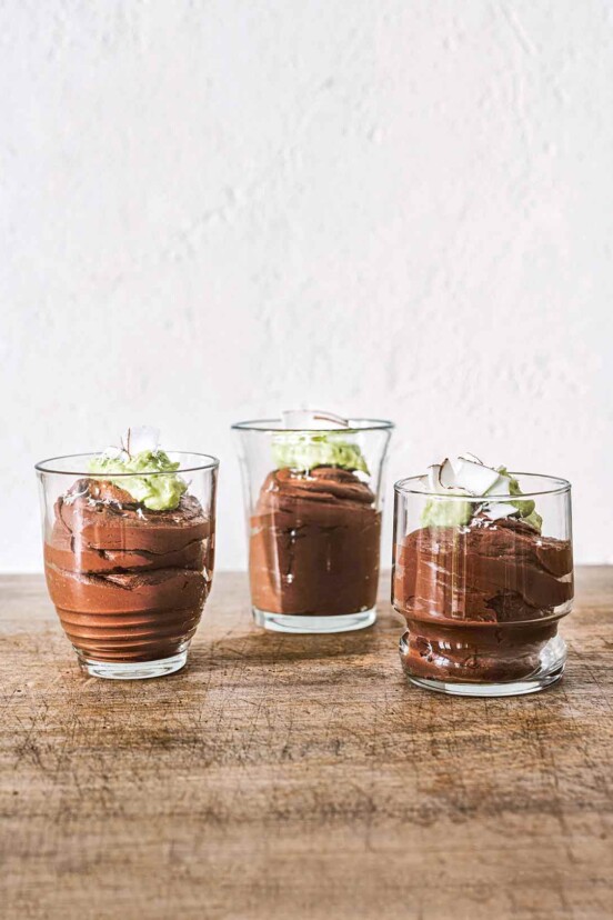 Chocolate avocado coconut mousse in three glasses, each garnished with avocado purée and coconut flakes.