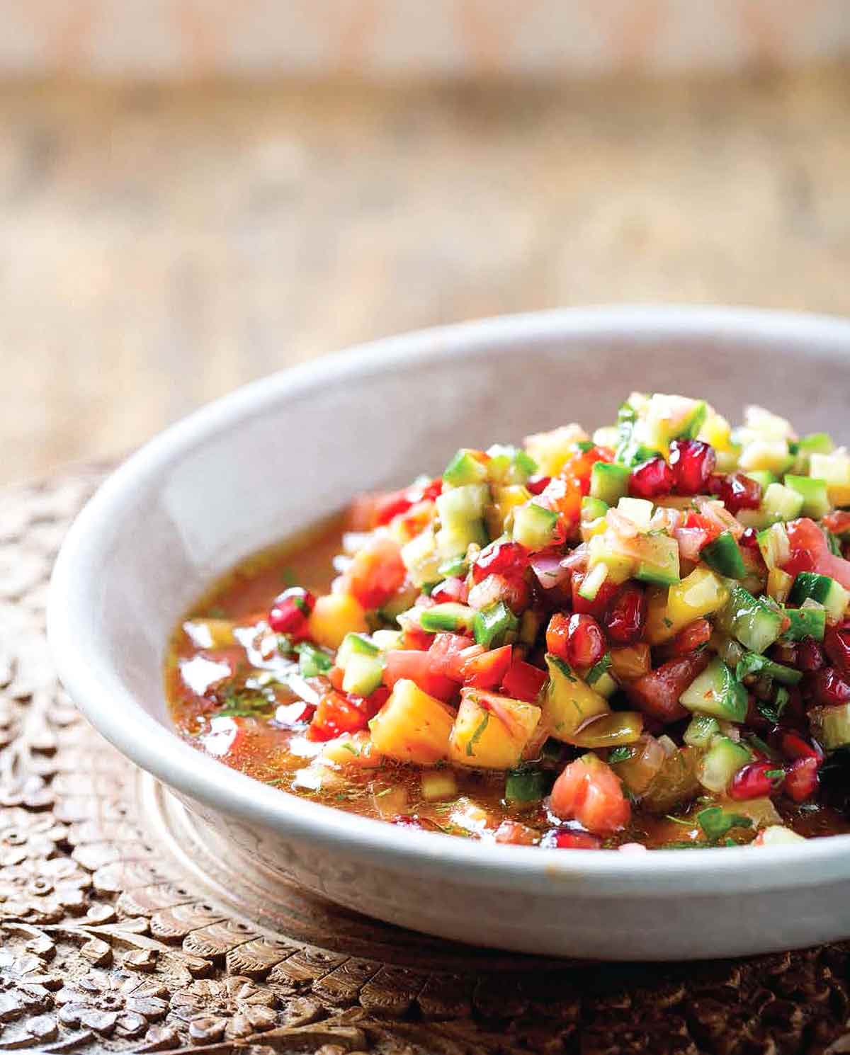 Chopped vegetable salad with pomegranate piled in a white bowl on a carved wooden tray.