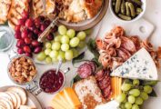 Classic cheese charcuterie board with grapes, spiced nuts, baked Brie, sliced meat, toasted baguette, gherkins, cheese and more.