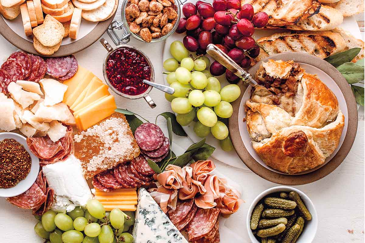 Classic cheese charcuterie board with grapes, spiced nuts, baked Brie, sliced meat, toasted baguette, gherkins, cheese and more.