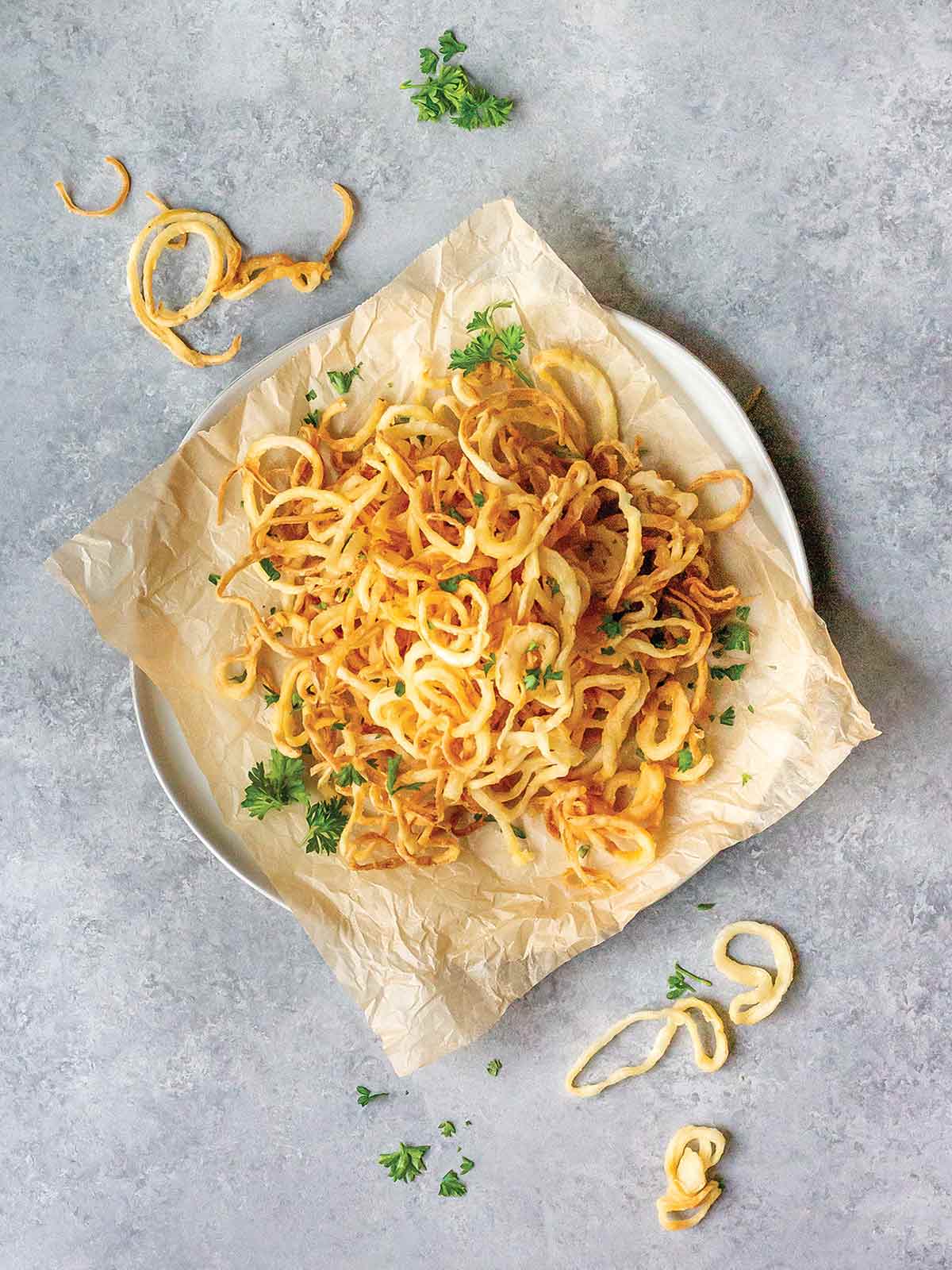 Dairy-free crispy onion strings on a sheet of parchment, on a white plate, garnished with parsley.