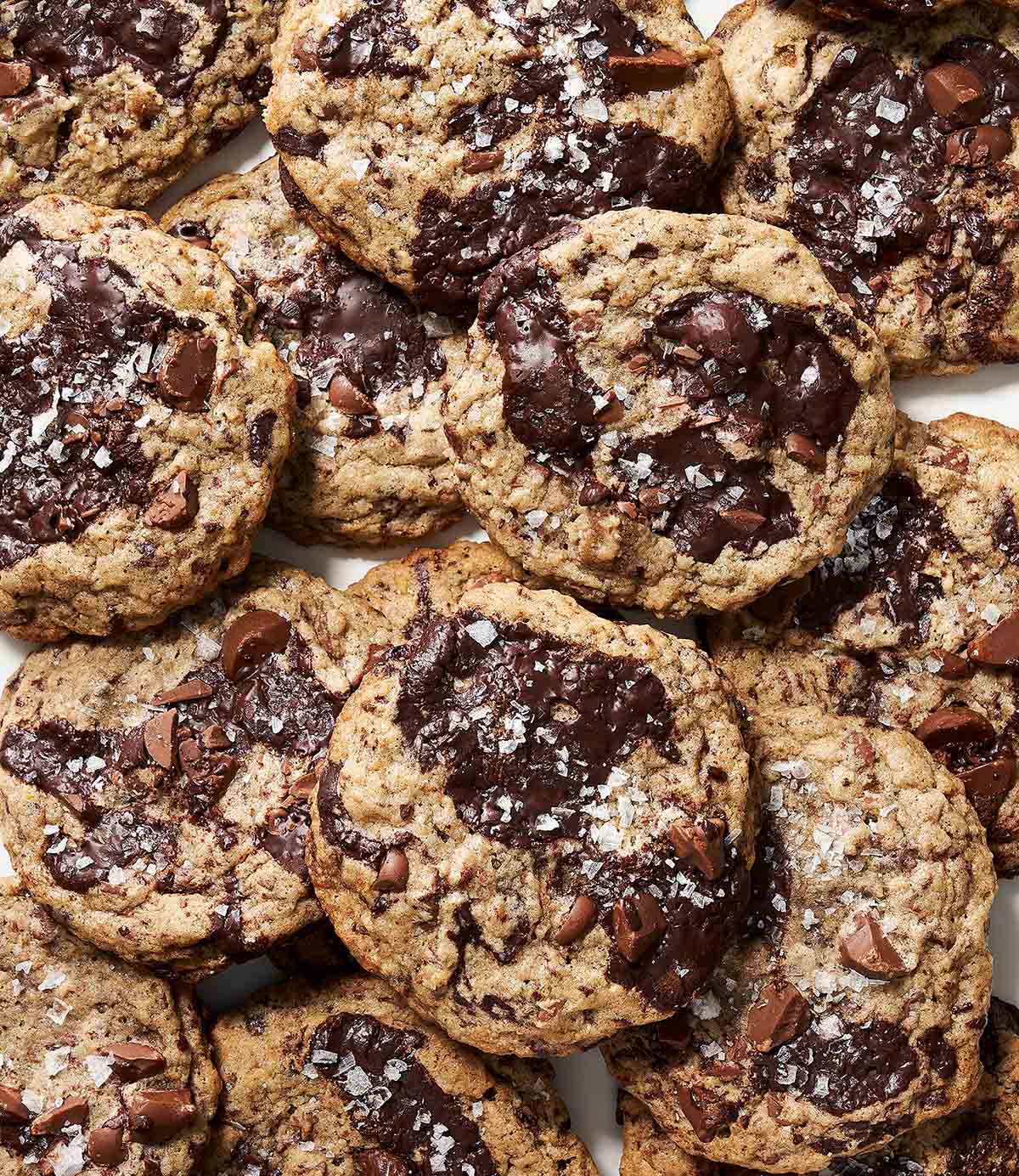 Double chocolate chunk sourdough cookies garnished with flaky salt, piled on a piece of parchment.