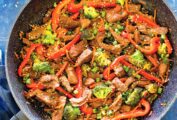 Easy beef stir fry, garnished with scallions and sesame seeds, in a large skillet on a counter.