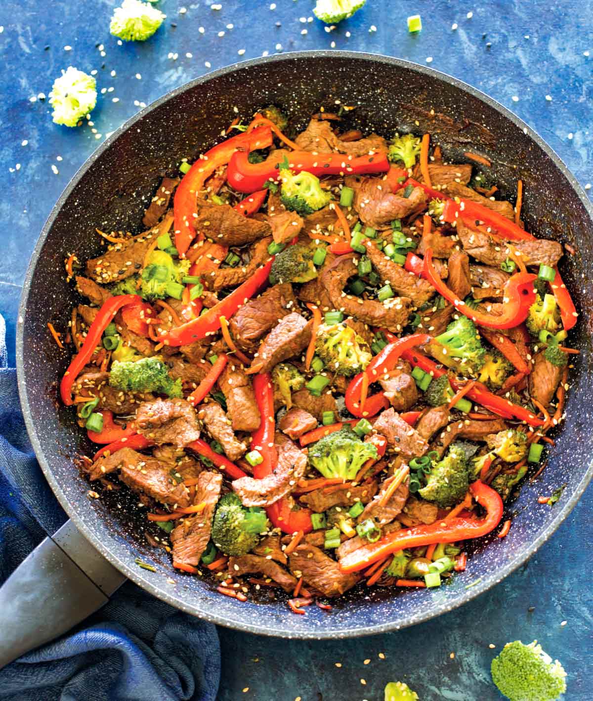 Easy beef stir fry, garnished with scallions and sesame seeds, in a large skillet on a counter.