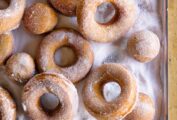 Easy Jewish Hanukkah doughnuts and doughnut holes covered with sugar, on a metal cookie sheet.