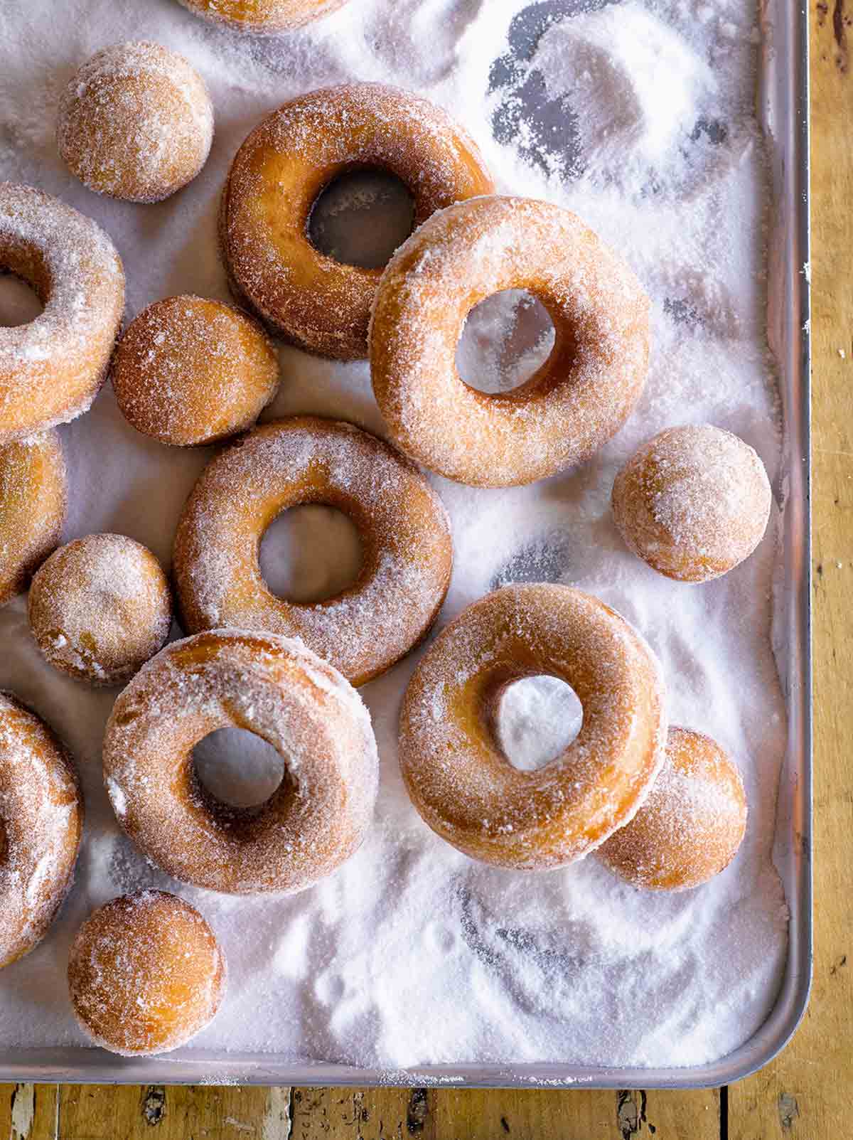 Easy Jewish Hanukkah doughnuts and doughnut holes covered with sugar, on a metal cookie sheet.