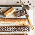 Espresso millionaire shortbread bars cut into long strips on a sheet of parchment paper on a cookies rack with a knife.