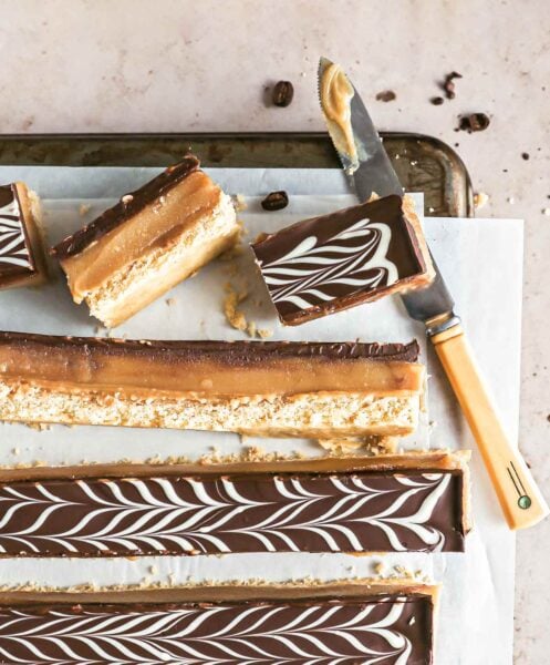 Espresso millionaire shortbread bars cut into long strips on a sheet of parchment paper on a cookies rack with a knife.