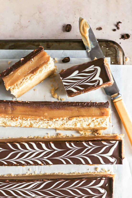 Espresso millionaire shortbread bars cut into long strips on a sheet of parchment paper on a cookies rack with a knife.