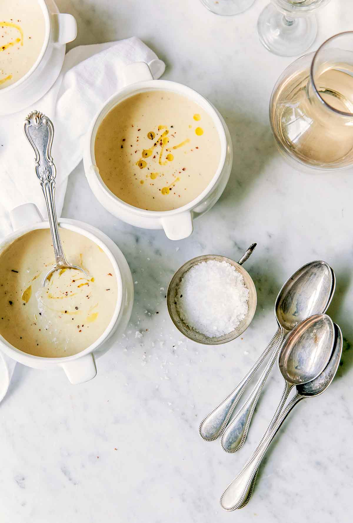 Three bowls of fennel potato soup, one with a soup spoon, beside a small bowl of salt.