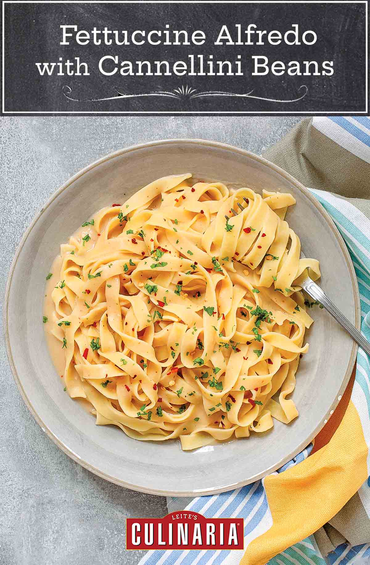 Fettuccine Alfredo with cannellini beans in a large white bowl with a fork, beside a striped cloth.