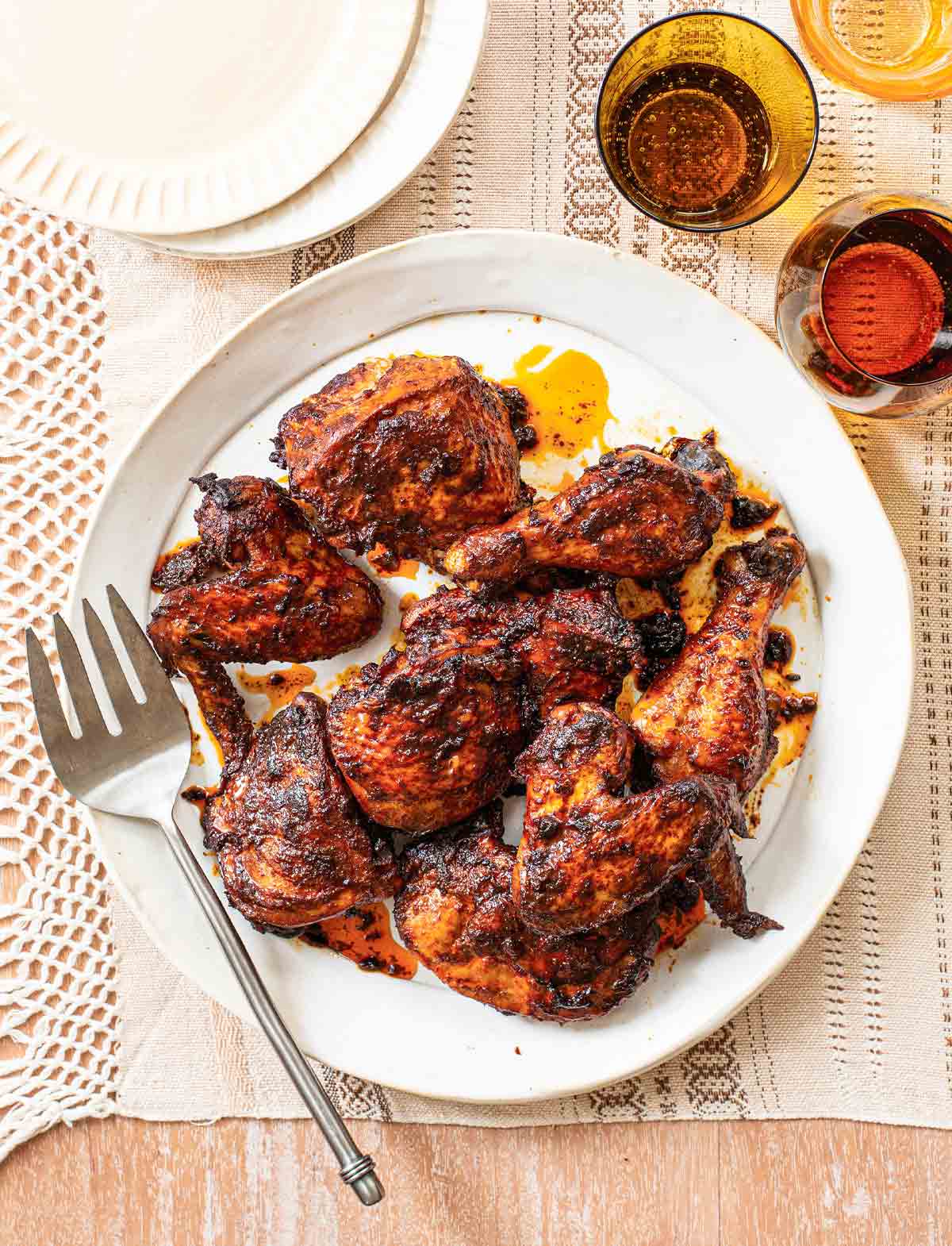 Garlic, chile, and cumin roast chicken on a white platter with a serving fork, beside empty plates and glasses of wine.