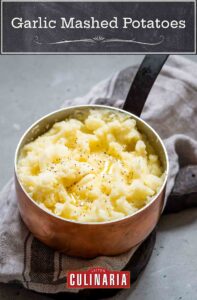Garlic mashed potatoes with melted butter and black pepper inside a copper pot, resting on a kitchen towel.