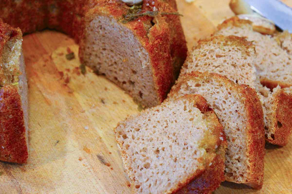 A close-up shot of Rosemary-Garlic Sourdough Bread made in a bundt pan, with slices of the bread in the foreground.