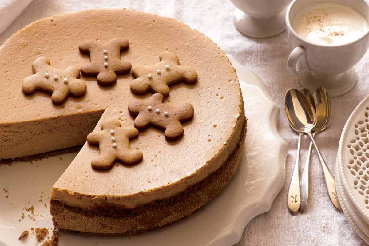 Gingerbread cookies, both molasses and honey, in a circle on top of a gingerbread cheesecake, beside cups of latte and spoons.