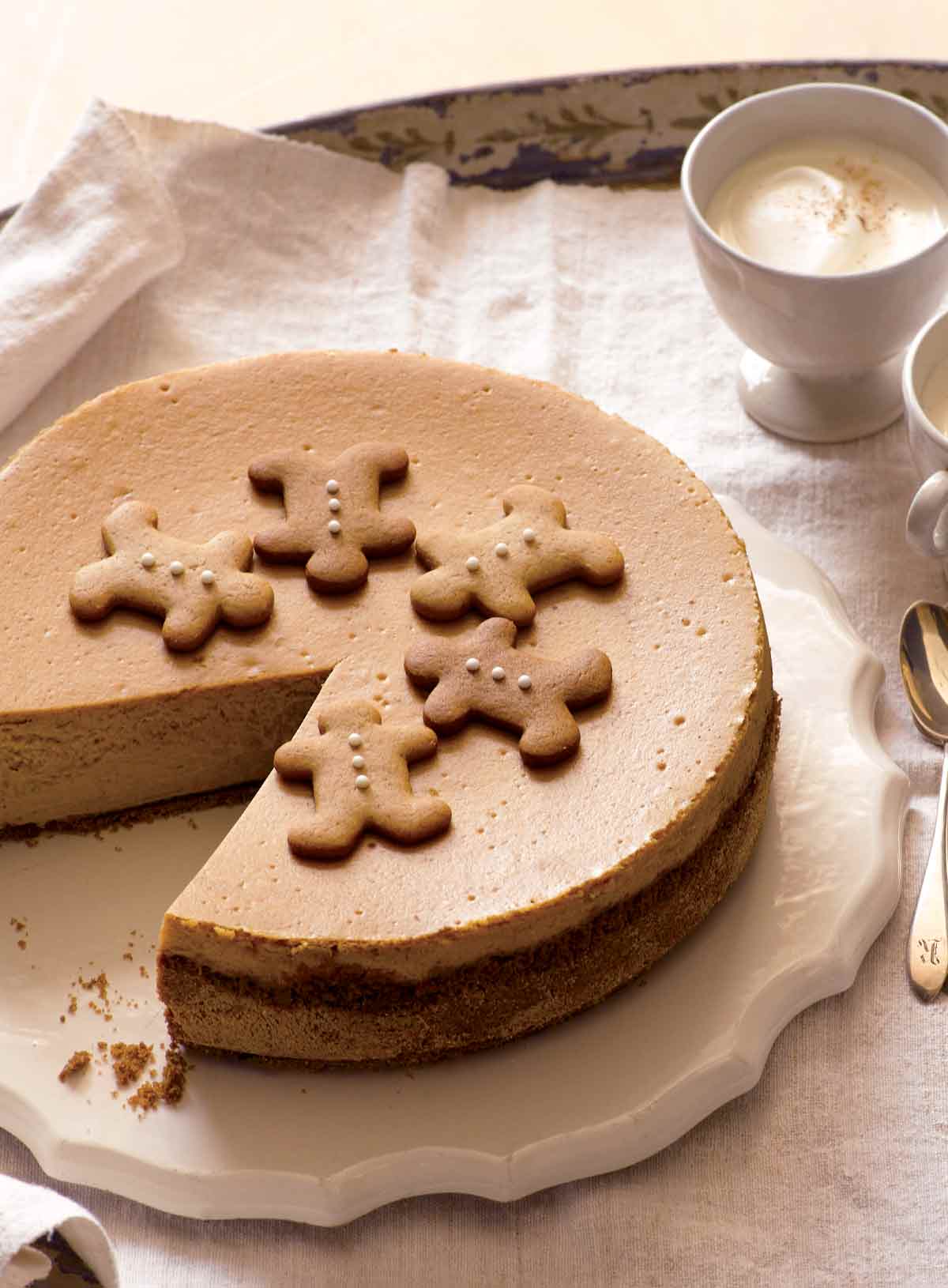Gingerbread cookies, both molasses and honey, in a circle on top of a gingerbread cheesecake, beside cups of latte and spoons.
