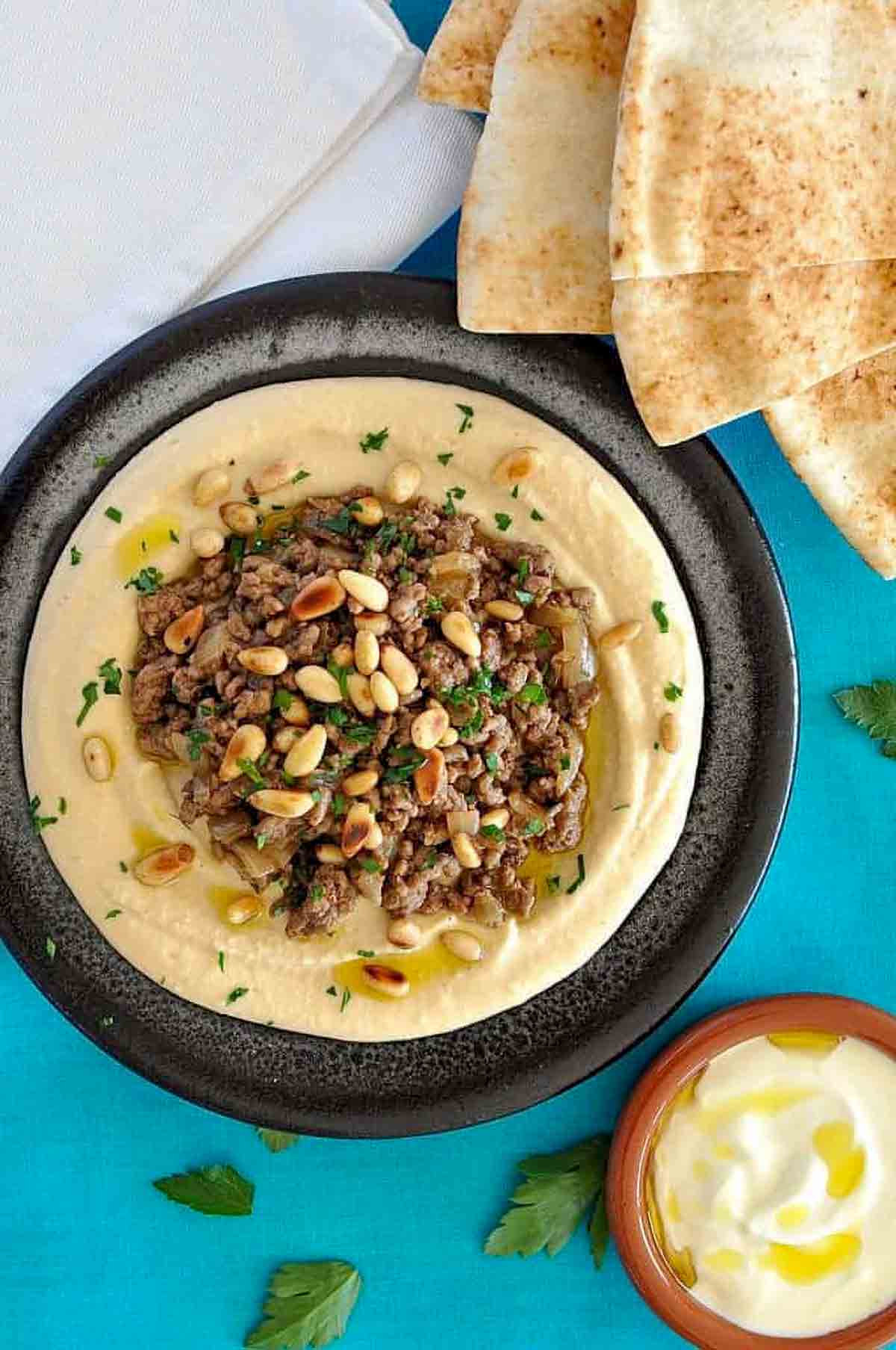 a bowl of Ottolenghi's hummus with lamb on a blue background