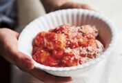 Italian style meatballs in a white bowl with grated cheese, being held over a table.