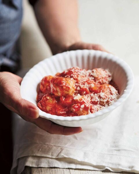 Italian style meatballs in a white bowl with grated cheese, being held over a table.