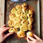 Jamie Oliver's Garlic Pull-Apart Rolls on a metal sheet pan, garnished with crispy bread crumbs, and being pulled apart by two hands.