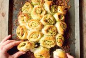 Jamie Oliver's Garlic Pull-Apart Rolls on a metal sheet pan, garnished with crispy bread crumbs, and being pulled apart by two hands.
