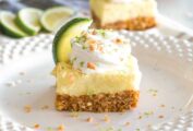 Key lime pie bars, cut into squares and garnished with whipped cream, lime zest, slices of lime, and chopped almonds.
