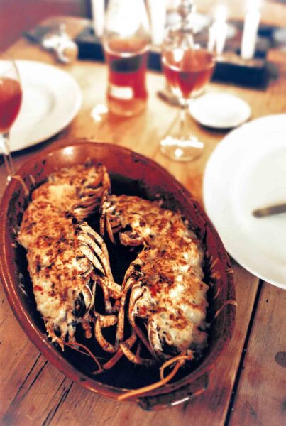 2 Lobster thermidor in a baking dish, flanked by dinner plates and glasses of wine.