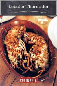 2 Lobster thermidor in a baking dish, flanked by dinner plates and glasses of wine.