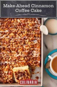 Make-ahead cinnamon coffee cake in a large rectangular pan, with two squares cut out, beside two cups of coffee and a bowl of drizzle with a spoon.