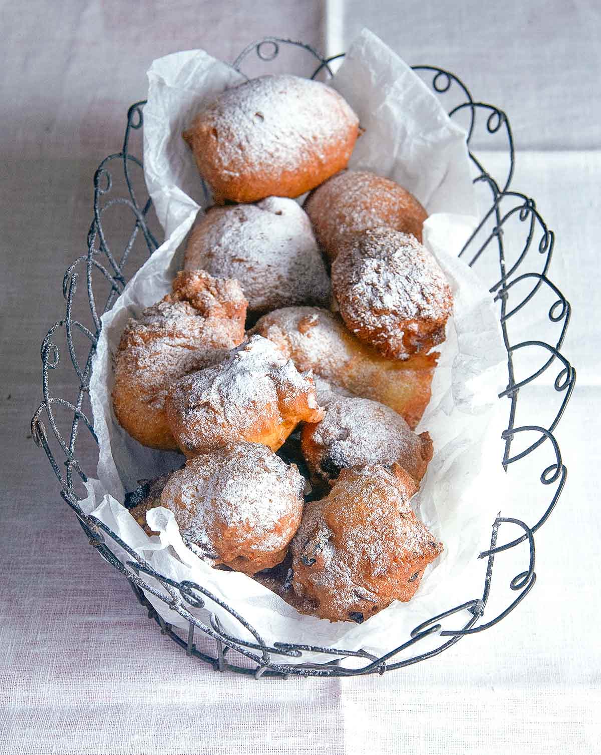 Oliebollen or Dutch doughnuts, in a wire basket, covered with powdered sugar on a white tablecloth.