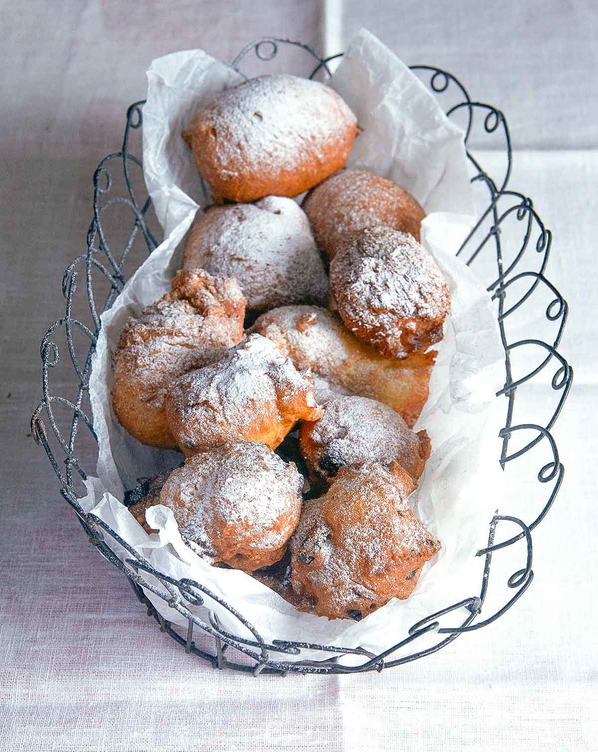 Oliebollen, or Dutch doughnuts, in a wire basket, covered with powdered sugar on a white tablecloth.