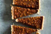 A rectangular pine nut-toffee tart with rosemary and orange cut into triangles