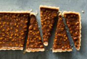 A rectangular pine nut-toffee tart with rosemary and orange cut into triangles