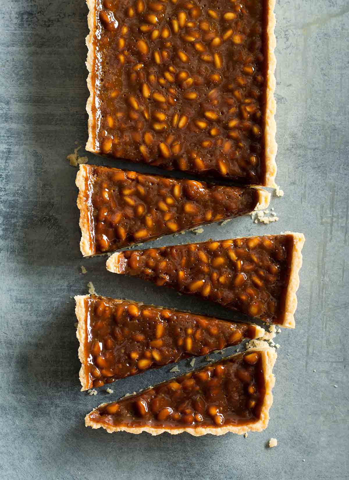 A rectangular pine nut-toffee tart with rosemary and orange cut into triangles