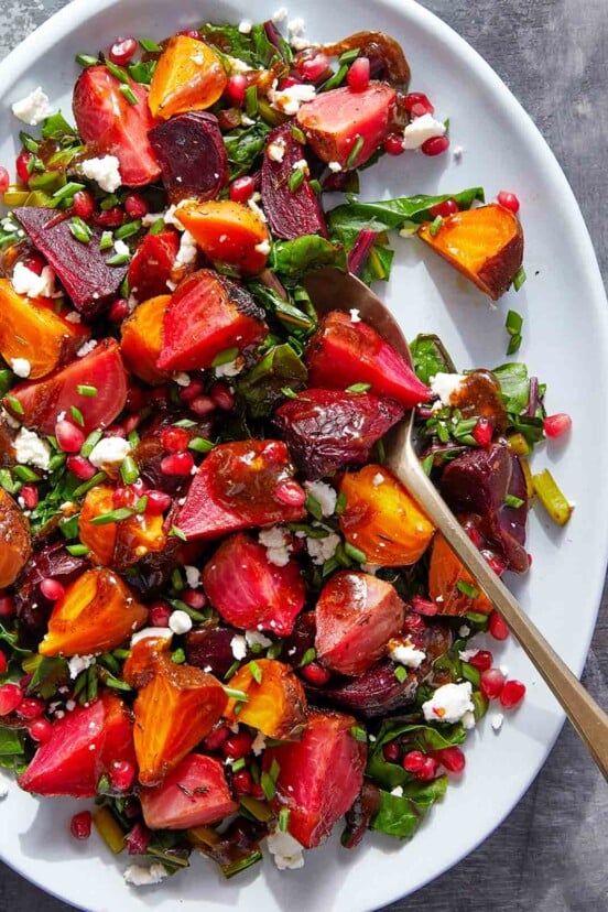 Pomegranate roasted beets with goat cheese on a large white serving plate, with a serving spoon.