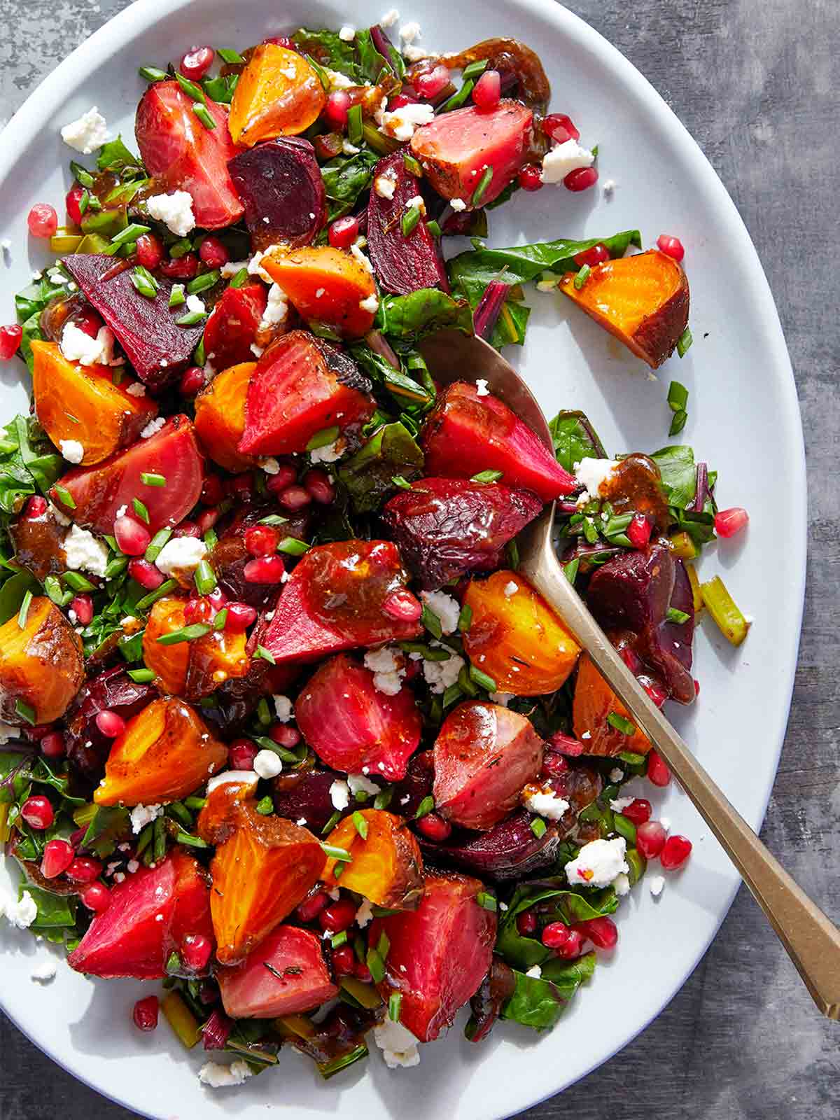 Pomegranate roasted beets with goat cheese on a large white serving plate, with a serving spoon.