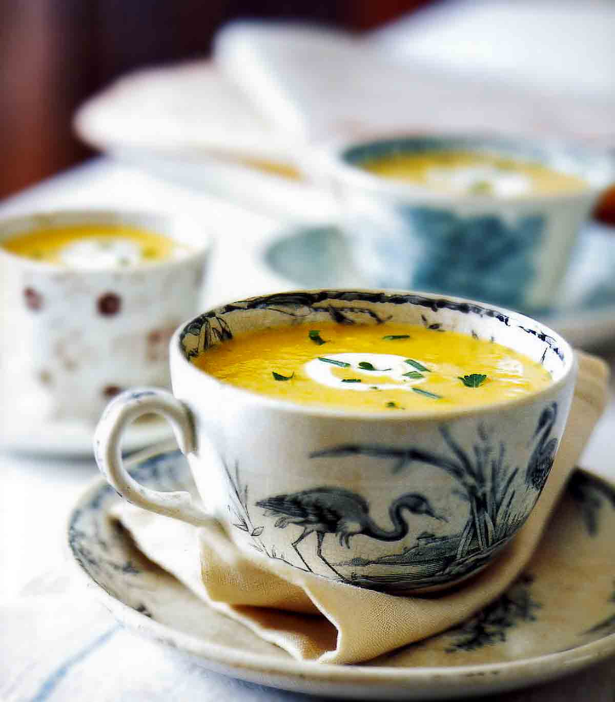 Pumpkin cider soup in a blue and white teacup, garnished with crème frâiche and chives.