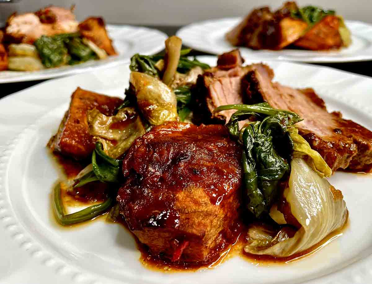 Three plates topped with roasted pork should er with mustard glaze and greens.