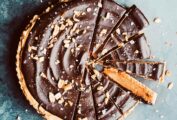 Salted chocolate peanut butter tart cut into slices, garnished with chopped peanuts.