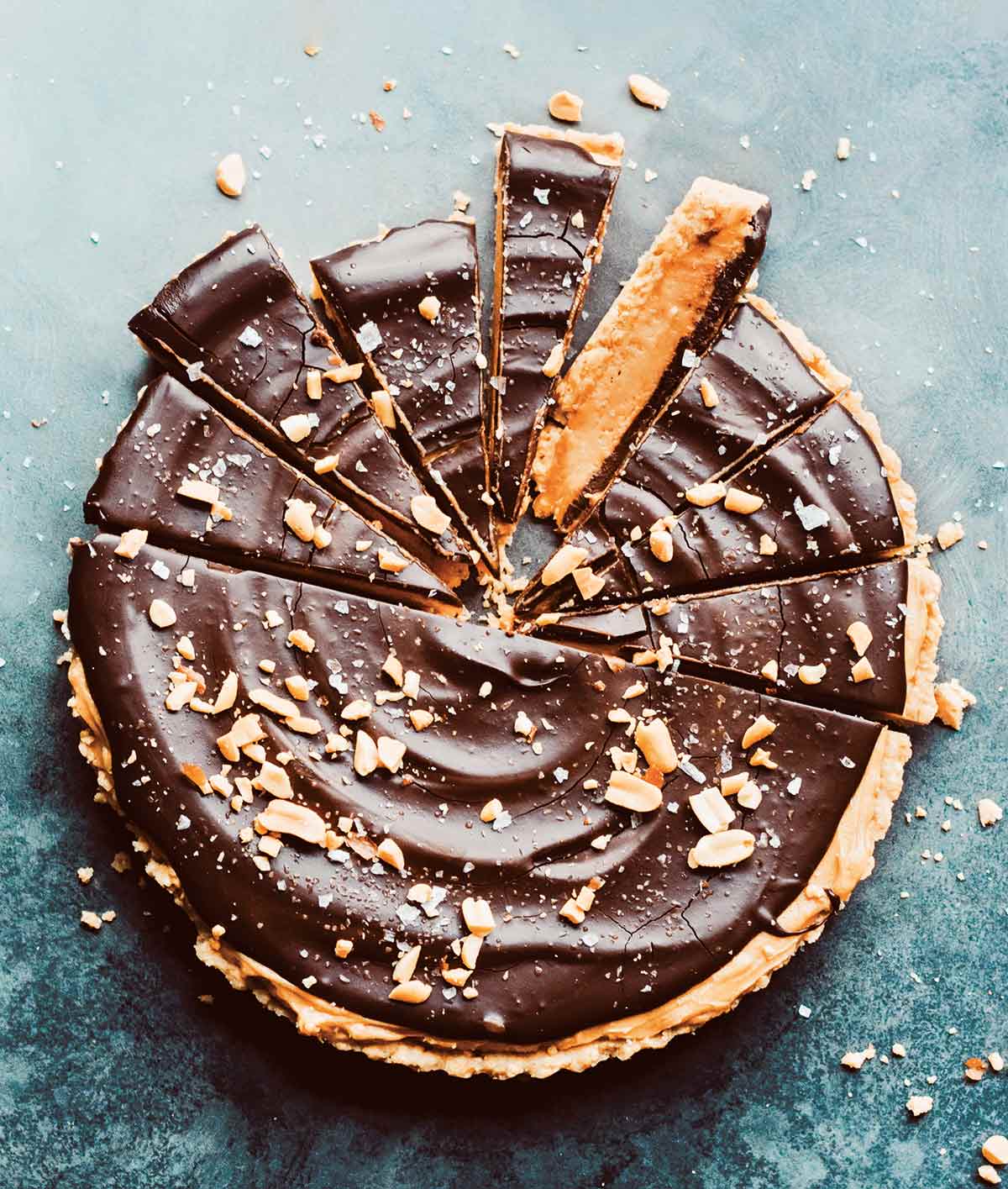 Salted chocolate and peanut butter tart cut into slices, garnished with chopped peanuts.