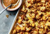 Sicilian-style roasted cauliflower on a sheet pan with a bowl of dressing.