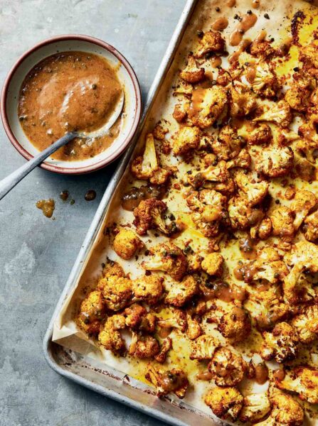 Sicilian-style roasted cauliflower on a sheet pan with a bowl of dressing.