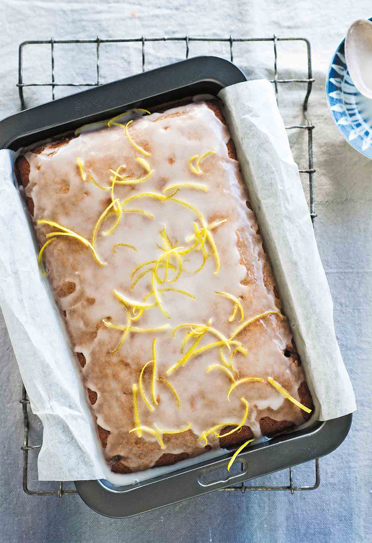 Spiced gingerbread with lemon glaze garnished with lemon zest strips, in a parchment-lined cake pan.