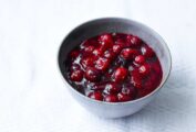 Spicy cranberry sauce in a grey pottery bowl on a white tablecloth, beside a serving spoon.