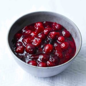 Spicy cranberry sauce in a grey pottery bowl on a white tablecloth, beside a serving spoon.