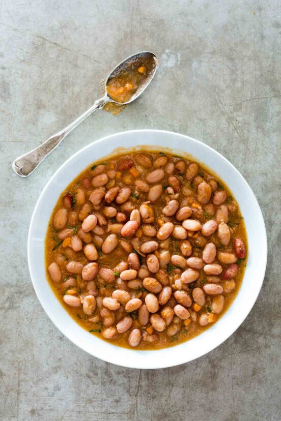 A white bowl filled with cranberry beans with warm spices; a spoon along side