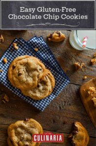 A wooden table with a blue check napkin and glass of milk with a straw. 6 easy gluten-free chocolate chip cookies, in whole and halves, are scattered on the table with crumbs.