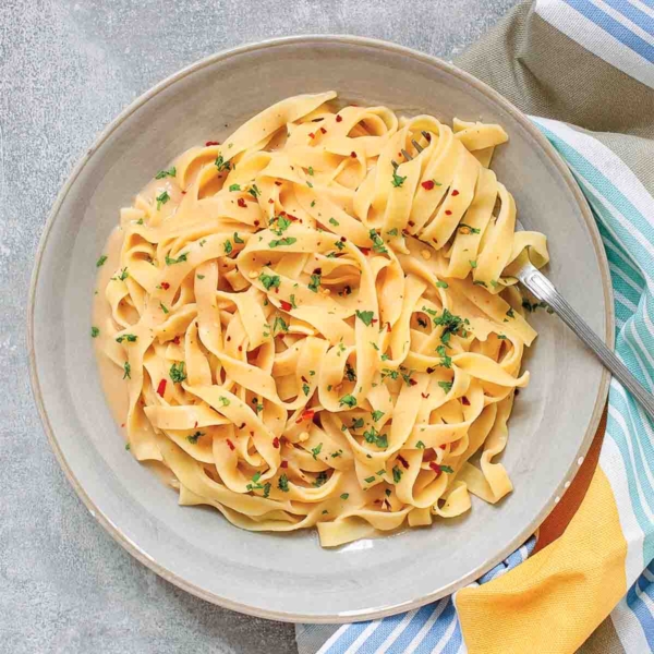 Fettuccine Alfredo with cannellini beans in a large white bowl with a fork, beside a striped cloth.