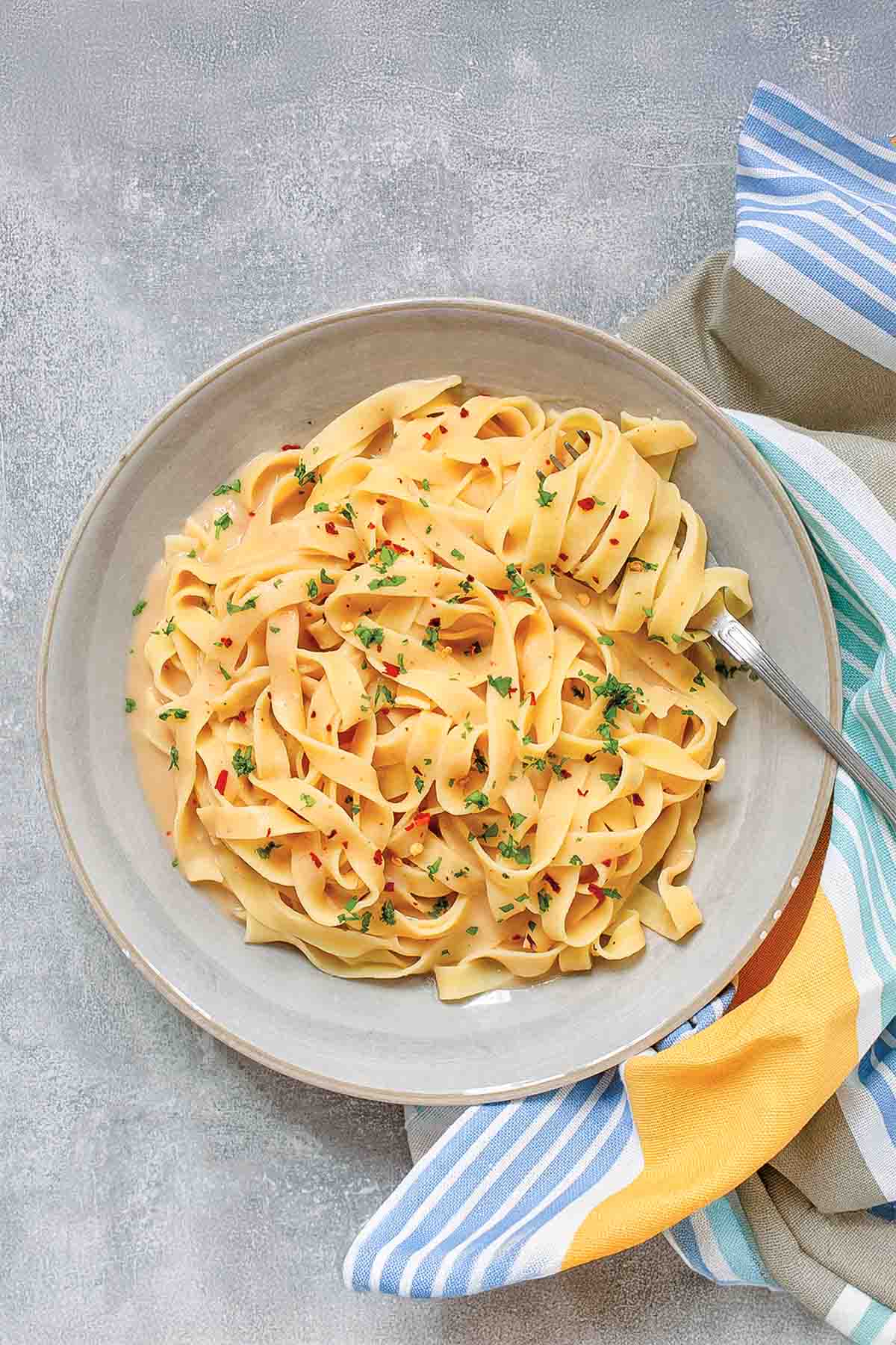 Fettuccine Alfredo with cannellini beans in a large white bowl with a fork, beside a striped cloth.